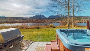 Ein Garten mit Whirlpool, Grill und Blick auf Berge und einen See.