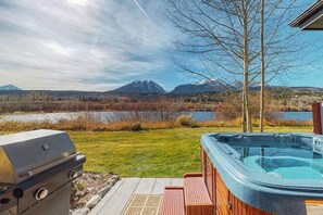A backyard with a hot tub, grill, and a view of mountains and a lake.