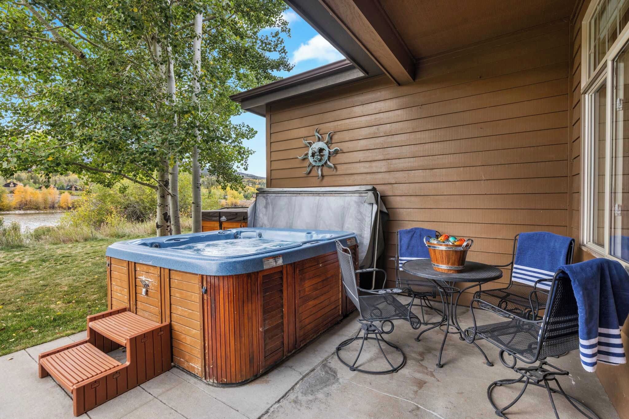 A hot tub with steps, a table, chairs, and a sun decoration on a wooden wall.