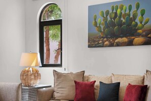 Ein Wohnzimmer mit einer Couch, Kissen, einer Lampe und einem Kakteenbild an der Wand.