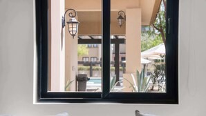 Ein Fenster mit Blick auf einen Außenpoolbereich, inklusive einer Pergola und Sonnenschirmen.