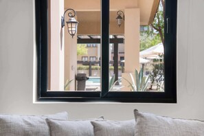 Ein Fenster mit Blick auf einen Außenpoolbereich, inklusive einer Pergola und Sonnenschirmen.