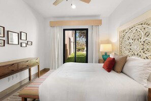 Quarto com cama, escrivaninha, cadeira, abajur e vista através de uma porta de vidro.