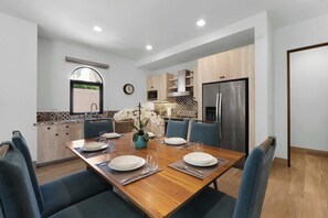 Eine moderne Küche mit Essbereich, Holzschränken, einem Edelstahlkühlschrank und einer Uhr an der Wand.