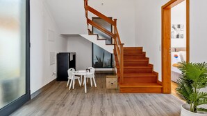 Un intérieur moderne avec un escalier en bois, un coin repas comprenant une table et des chaises, et une grande fenêtre.