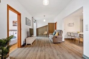 A modern living room with a sofa, a dining area with chairs, and a kitchen visible in the background. - Villa Brava Sunset by Homie (Ribeira Brava)