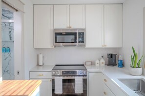 Eine moderne Küche mit weißen Schränken, einer Edelstahl-Mikrowelle, einem Gasherd, einer Kaffeemaschine und einem Blumentopf.