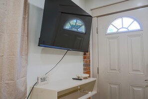 Una habitación con televisión montada, una puerta con ventana y una pared decorativa de ladrillo.