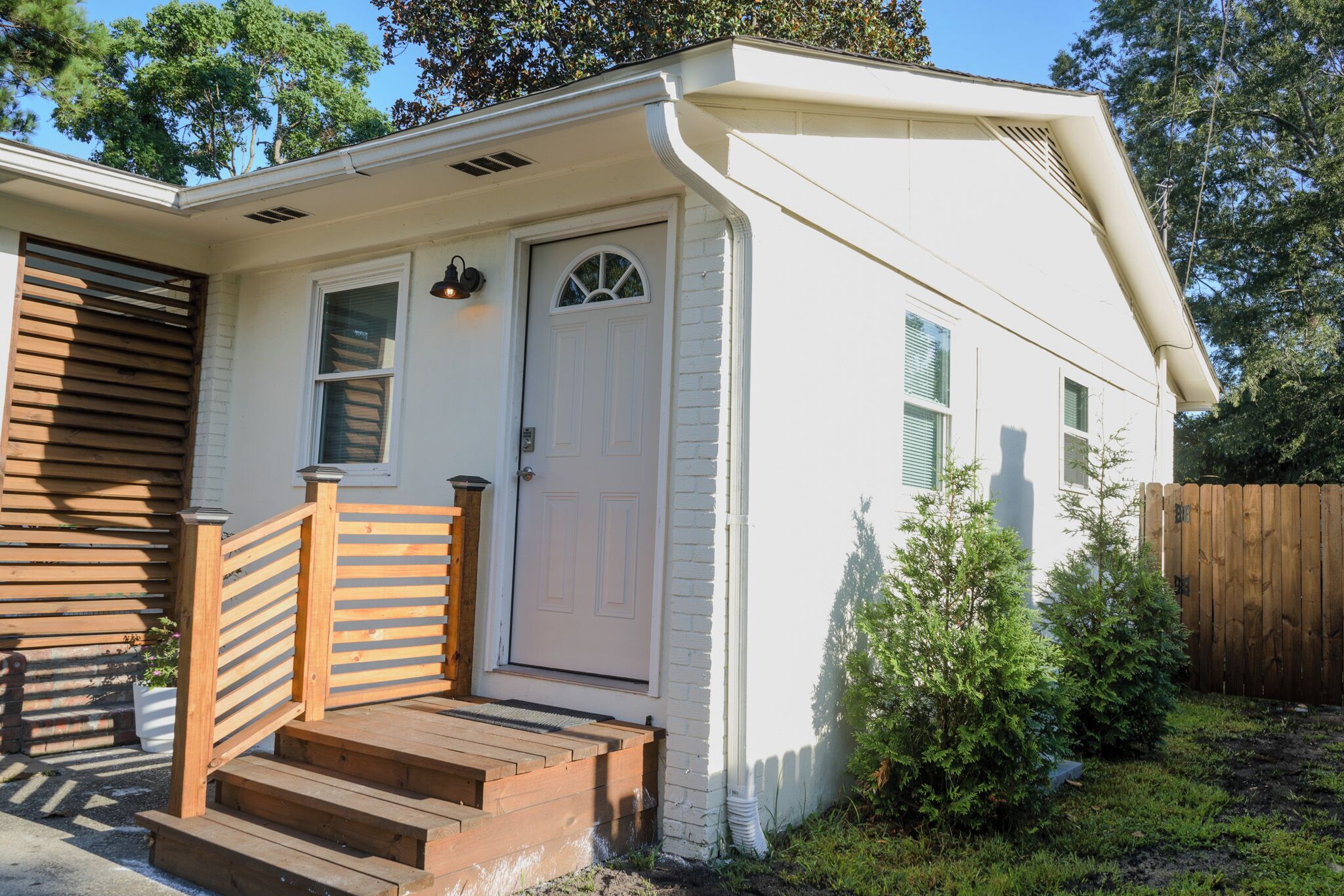 A small, single-story house with a front door, a small porch with steps, and a wooden fence in the background.