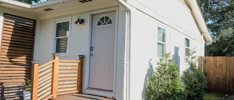 Une petite maison de plain-pied, avec une porte d’entrée, un petit porche avec des marches et une clôture en bois à l’arrière.