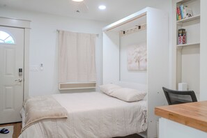 A bedroom with a bed, a window with a curtain, a bookshelf, and a desk.