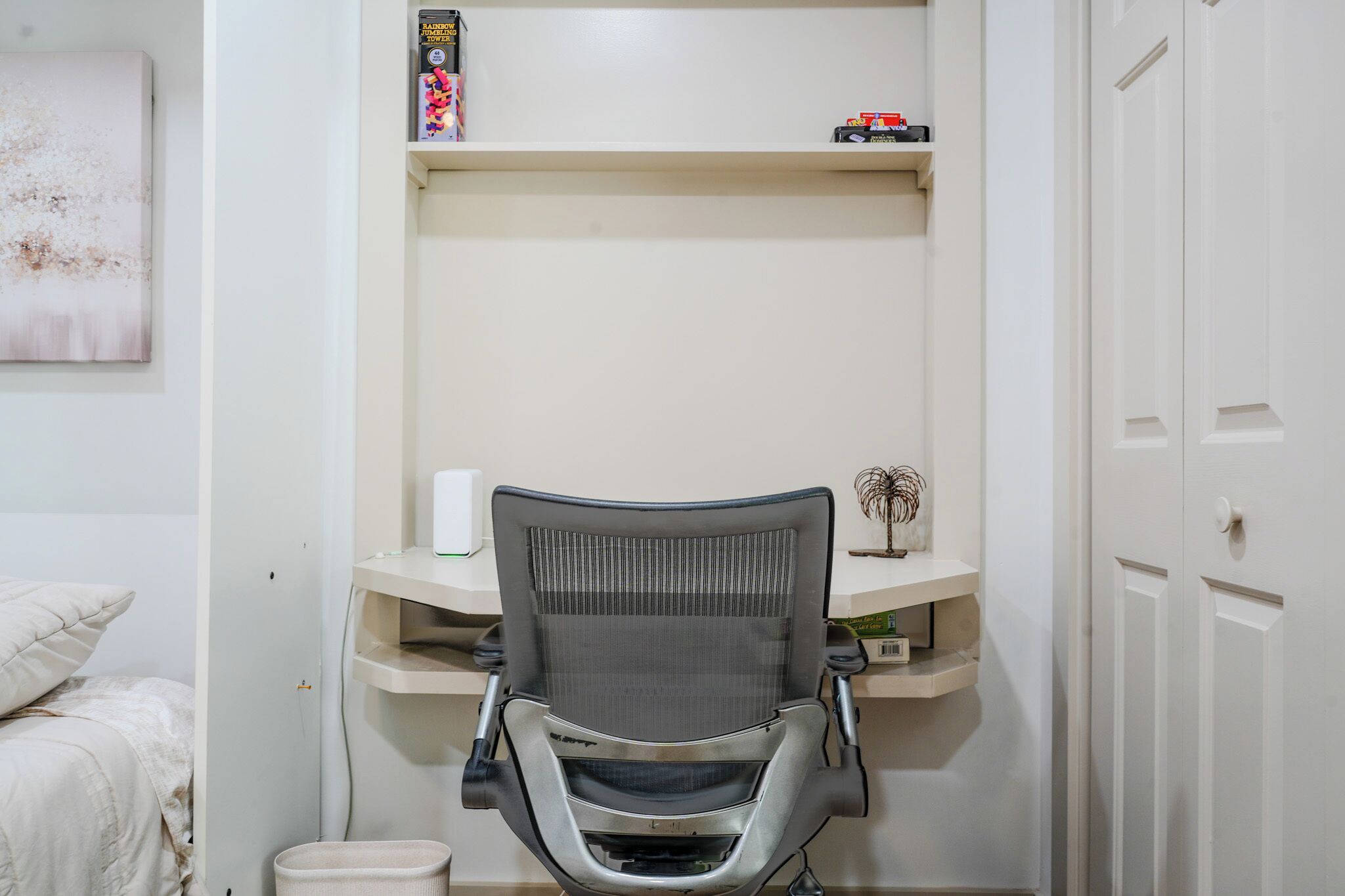 Une pièce comprenant un lit, un bureau avec une chaise, une étagère avec des livres et un objet décoratif, ainsi qu’une porte.