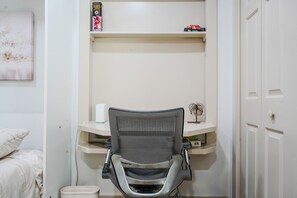 Una habitación con cama, escritorio y silla, estante con libros y un objeto decorativo, y una puerta.