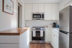 Una cocina moderna con armarios blancos, un refrigerador de acero inoxidable, un horno empotrado y un microondas sobre la estufa.