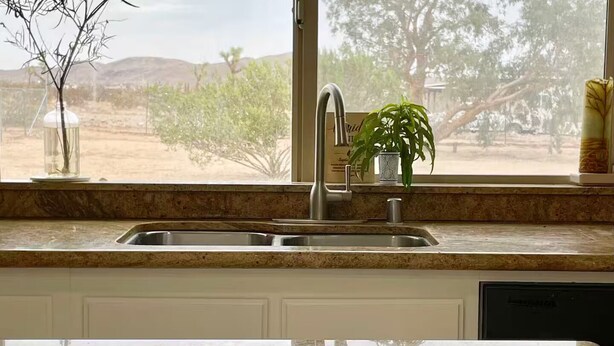 Una cocina con un lavamanos doble, una ventana que ofrece vistas a un paisaje desértico y una planta en maceta sobre el alféizar.