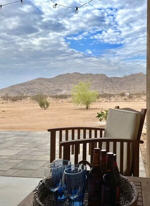 Eine Terrasse mit Blick auf eine Wüstenlandschaft, ein Holzstuhl und ein Tisch mit Gläsern und Flaschen.
