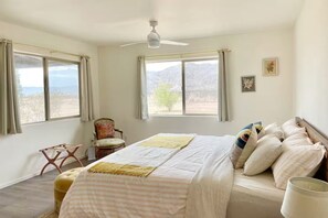 A bedroom with a bed, a chair, a ceiling fan, and two windows with curtains. - Queen of the Desert, 2 acres with expansive views (Joshua Tree)