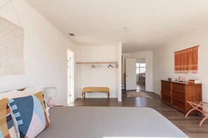Ein Schlafzimmer mit einem großen Bett, einer Sitzbank, einem Kleiderschrank und einem Flur, der in einen Essbereich führt.