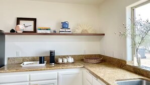 Una cocina con encimeras de granito, armarios blancos, una estantería empotrada con objetos decorativos y una ventana con vistas.