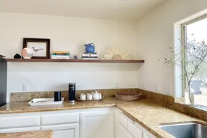 A kitchen with granite countertops, white cabinets, a built-in shelf with decorative items, and a window with a view. - Queen of the Desert, 2 acres with expansive views (Joshua Tree)
