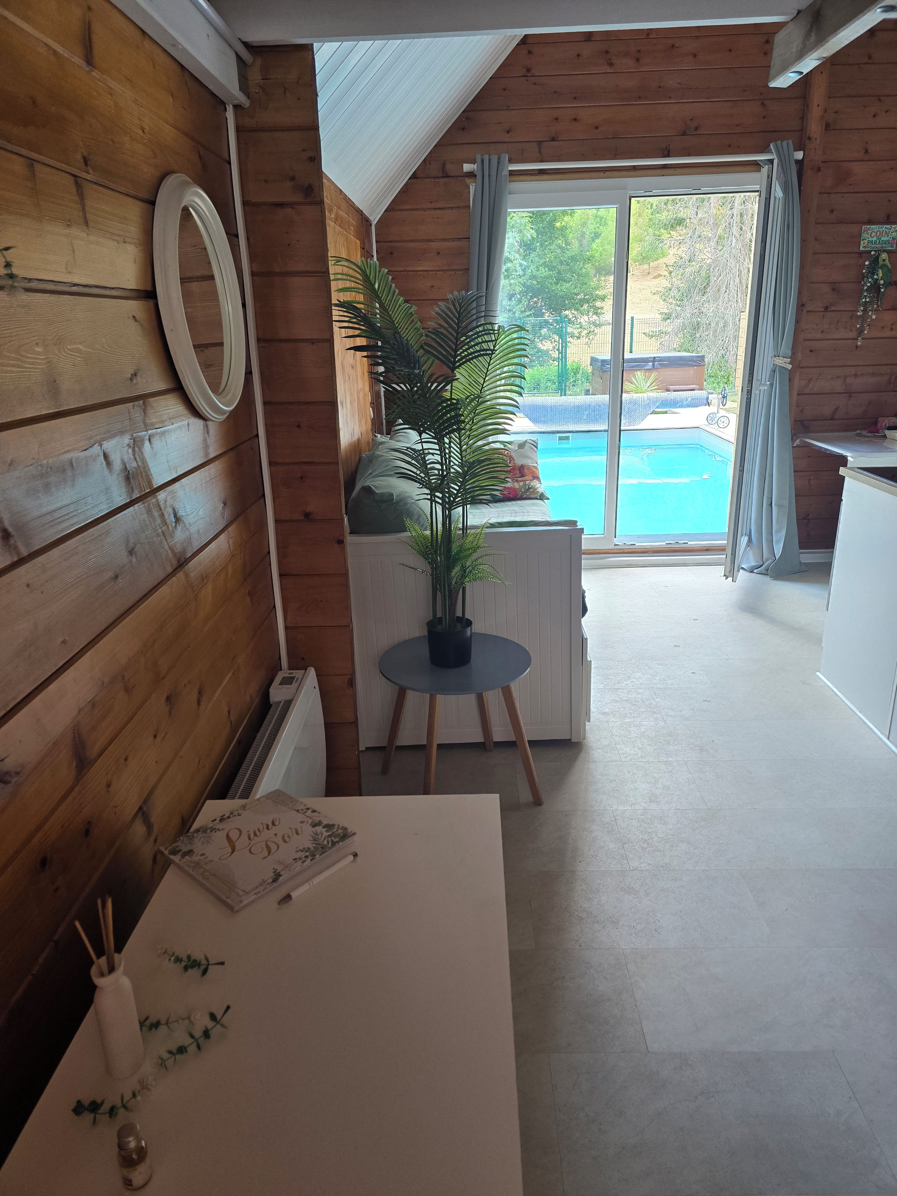 Ein Holzinterieur mit einem Esstisch, einem Blumentopf und Blick auf ein Außenbecken.