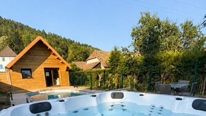 A hot tub with multiple jets, surrounded by a wooden deck and a house with a sloped roof.