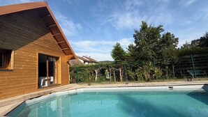 A wooden cabin with a pool, surrounded by trees and a fenced area.