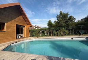 A wooden cabin with a pool, surrounded by trees and a fenced area.