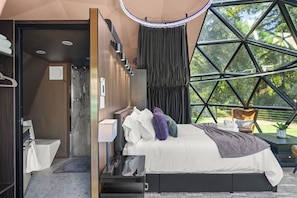 Ein modernes Schlafzimmer mit einem großen Bett, einer Dusche und Blick durch ein geometrisches Fenster.