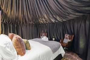 A room with a bed, two leather chairs, a small table with a plant, and a draped ceiling. - Evergreen Escape | Private Glass Dome, Sauna & Forest Views (Redmond)
