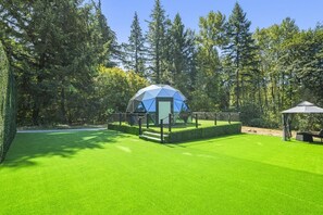A dome-shaped structure with a staircase leading up to it, surrounded by a well-manicured lawn and tall trees.