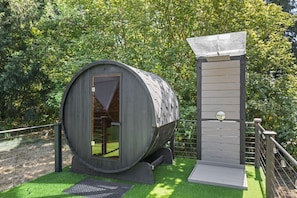 A cylindrical structure with a door and a vertical panel, surrounded by a fence and greenery. - Evergreen Escape | Private Glass Dome, Sauna & Forest Views (Redmond)