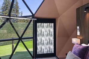 A modern room with a large window, a door with a forest pattern, a lamp, and a purple cushion.