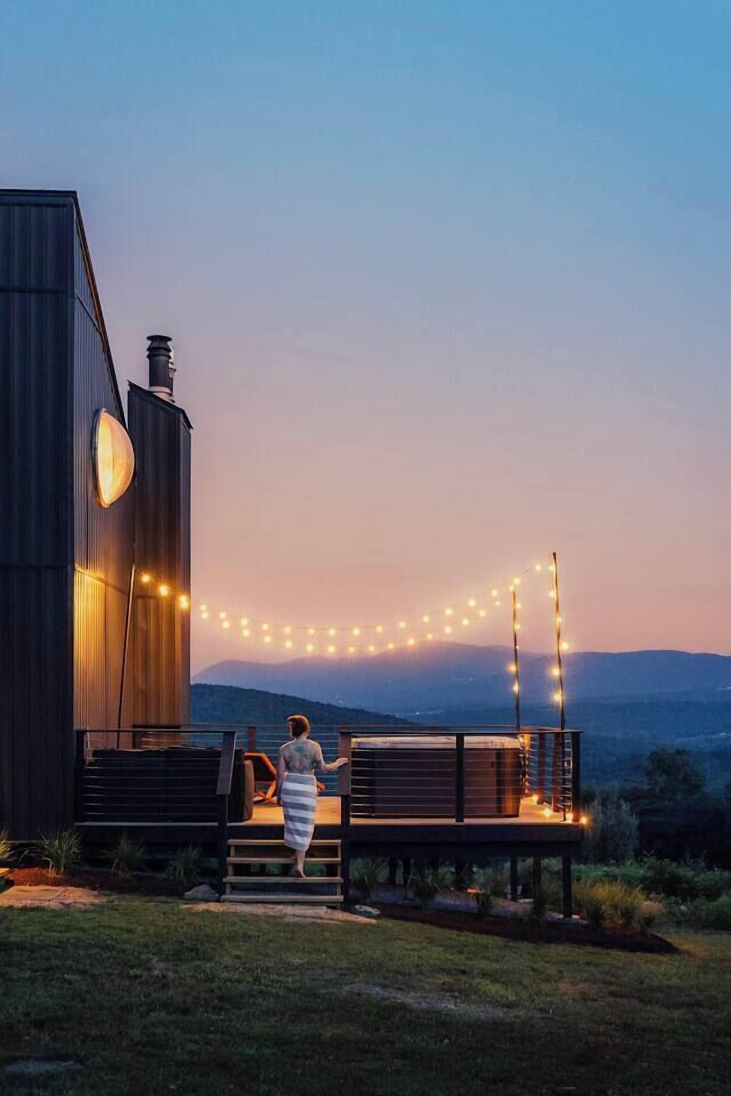 Ein modernes Gebäude mit einer Terrasse und Lichterketten, mit Blick auf eine hügelige Landschaft.