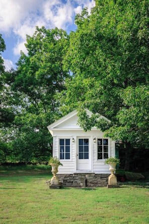 A small white house with a stone foundation, surrounded by lush green trees and grass. - Hollow Sky: 110 Acres, Hot Tub & Views (Rensselaerville)