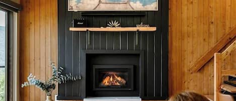 A cozy living room with a fireplace, wooden walls, and a painting of birds.