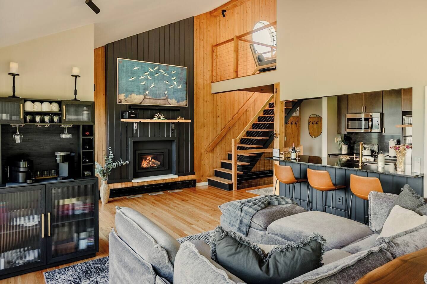 A modern living room with a fireplace, a staircase, and a kitchen area.