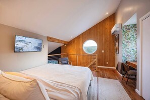 A bedroom with a large bed, a desk, a chair, a staircase, and a view through a window. - Hollow Sky: 110 Acres, Hot Tub & Views (Rensselaerville)