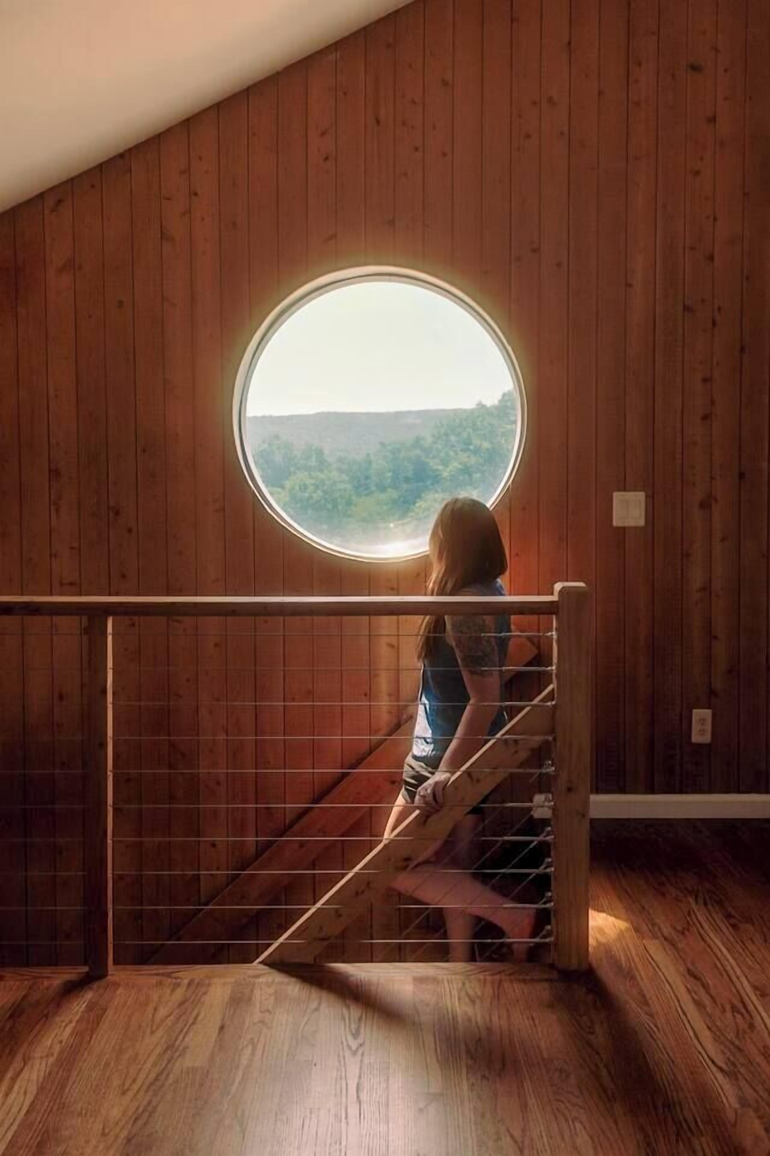 A wooden interior with a circular window overlooking a forested area.