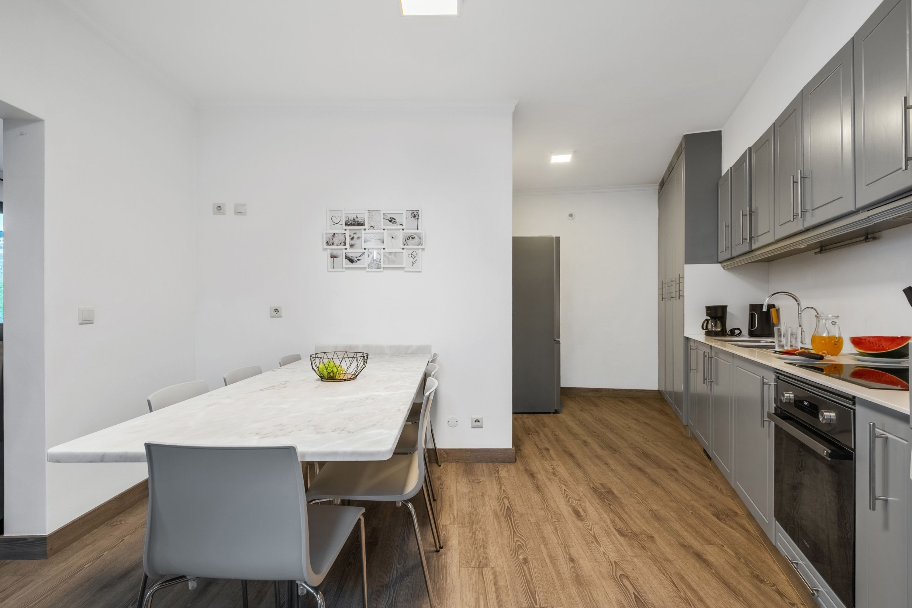 A modern kitchen with grey cabinets, a marble countertop, and a dining area with a white table and chairs.