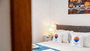 Hotellihuone, jossa on sänky, tyynyjä, yöpöytä, lamppu ja taulu seinällä.