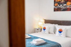 A hotel room with a bed, pillows, a nightstand, a lamp, and a painting on the wall. - Villa Brava Sunset by Homie (Ribeira Brava)