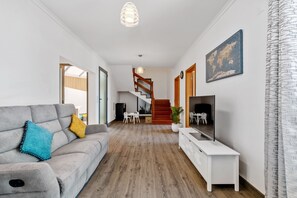 A modern living room with a grey sofa, a white TV stand, and a staircase leading to another level. - Villa Brava Sunset by Homie (Ribeira Brava)