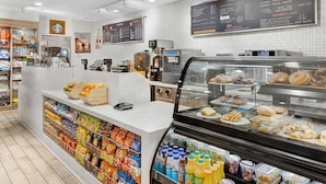 Mostrador de panadería con pasteles, un refrigerador con bebidas y una máquina de café.