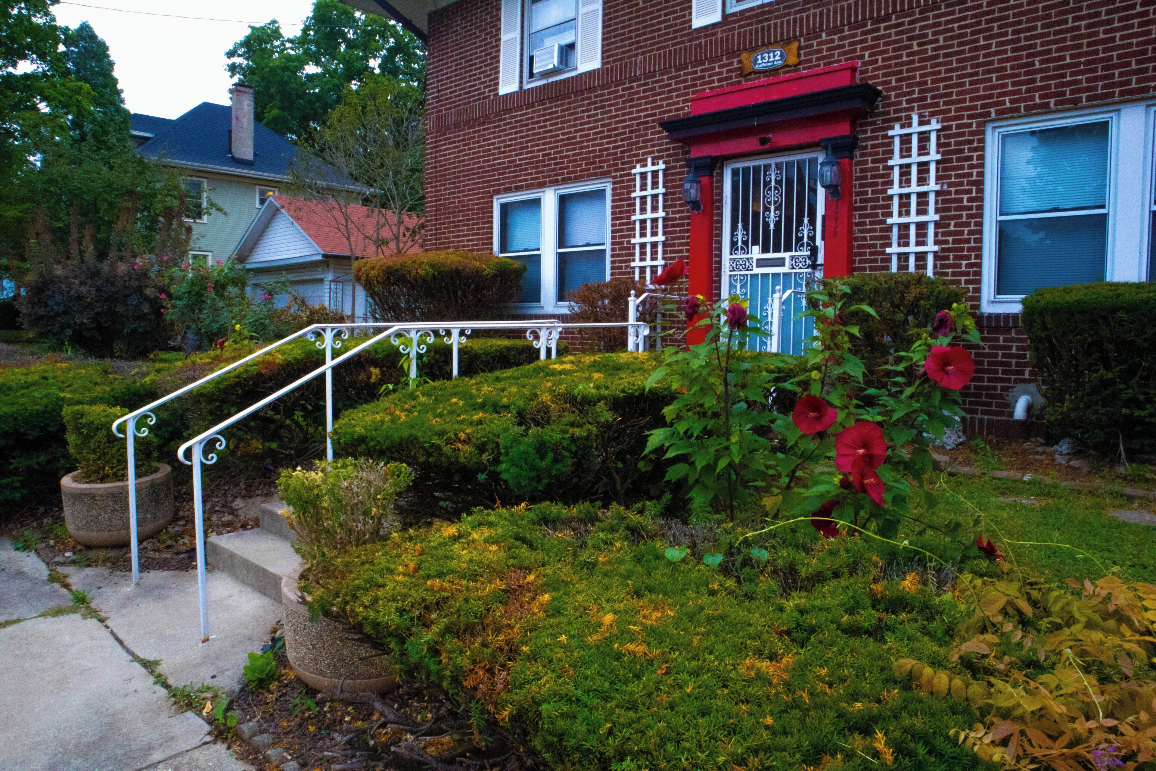 A red brick house with a white front door, a red porch, and a small garden with red flowers.
