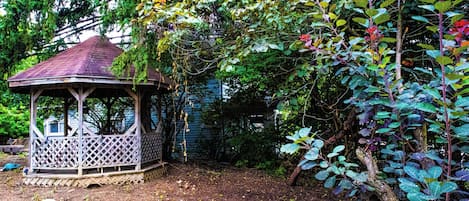 A gazebo with a lattice roof, surrounded by dense foliage and a wooden deck.