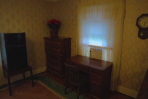 A room with a wooden desk, a chair, a dresser, and a clock on the wall.