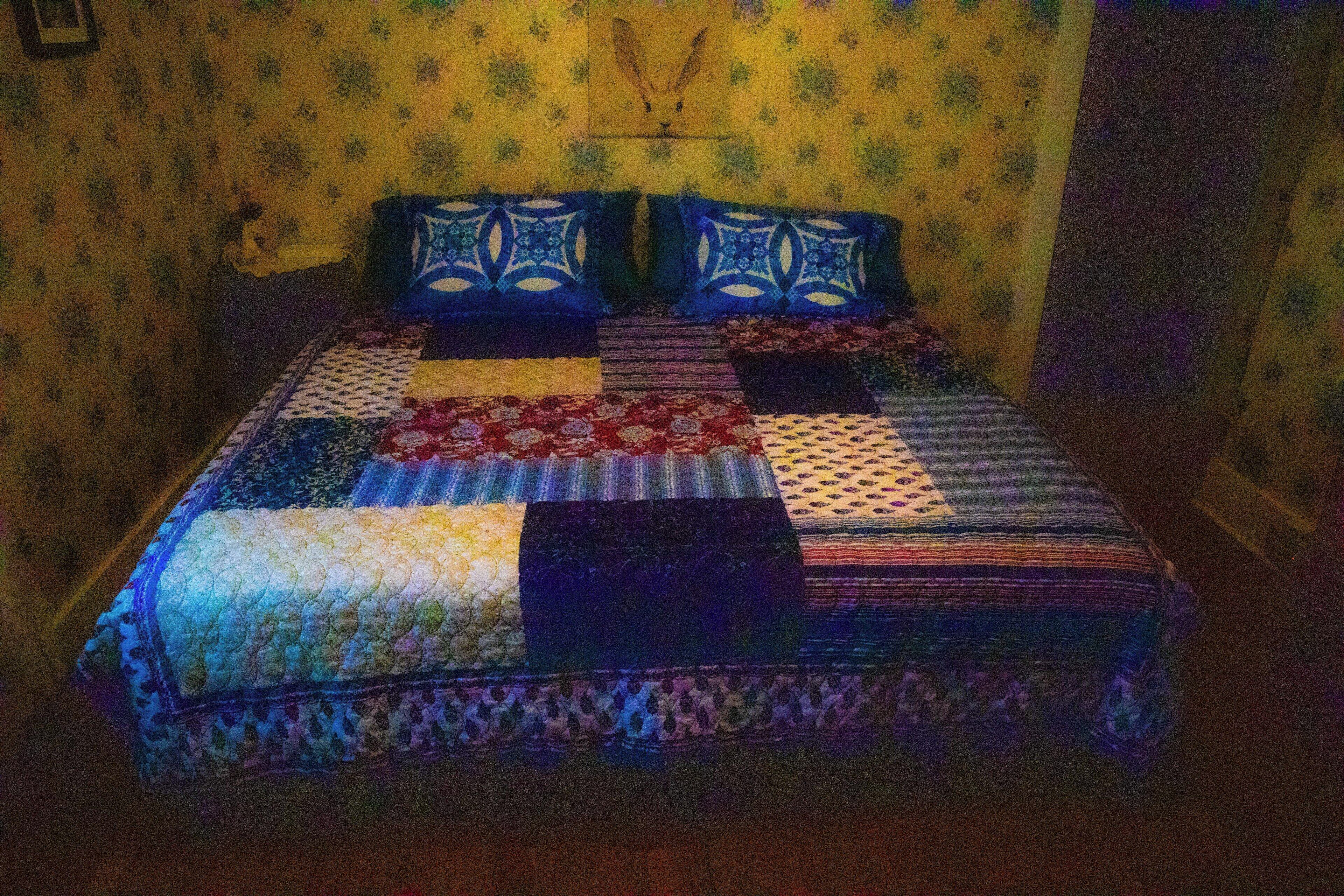 A bed with a patchwork quilt, a headboard, and a wall with a floral pattern.