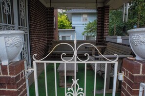 A gated patio area with a bench and a small table, surrounded by brick walls and a blue house in the background.