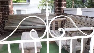 A covered patio area with a white metal fence, a wooden bench, and a table.
